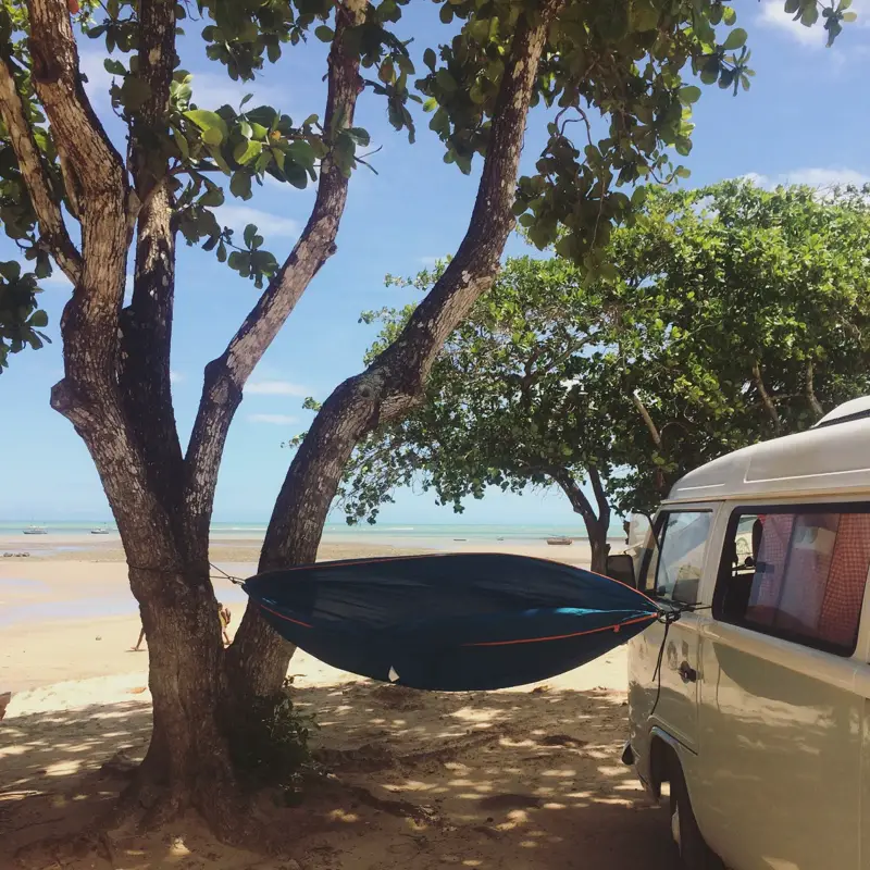 Kombi Camper RJ estacionada na praia, com rede armada na árvore